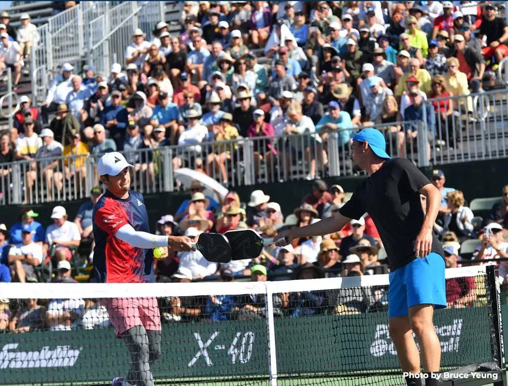 Deux joueurs de Pickleball tapotent leurs pagaies l'un contre l'autre.