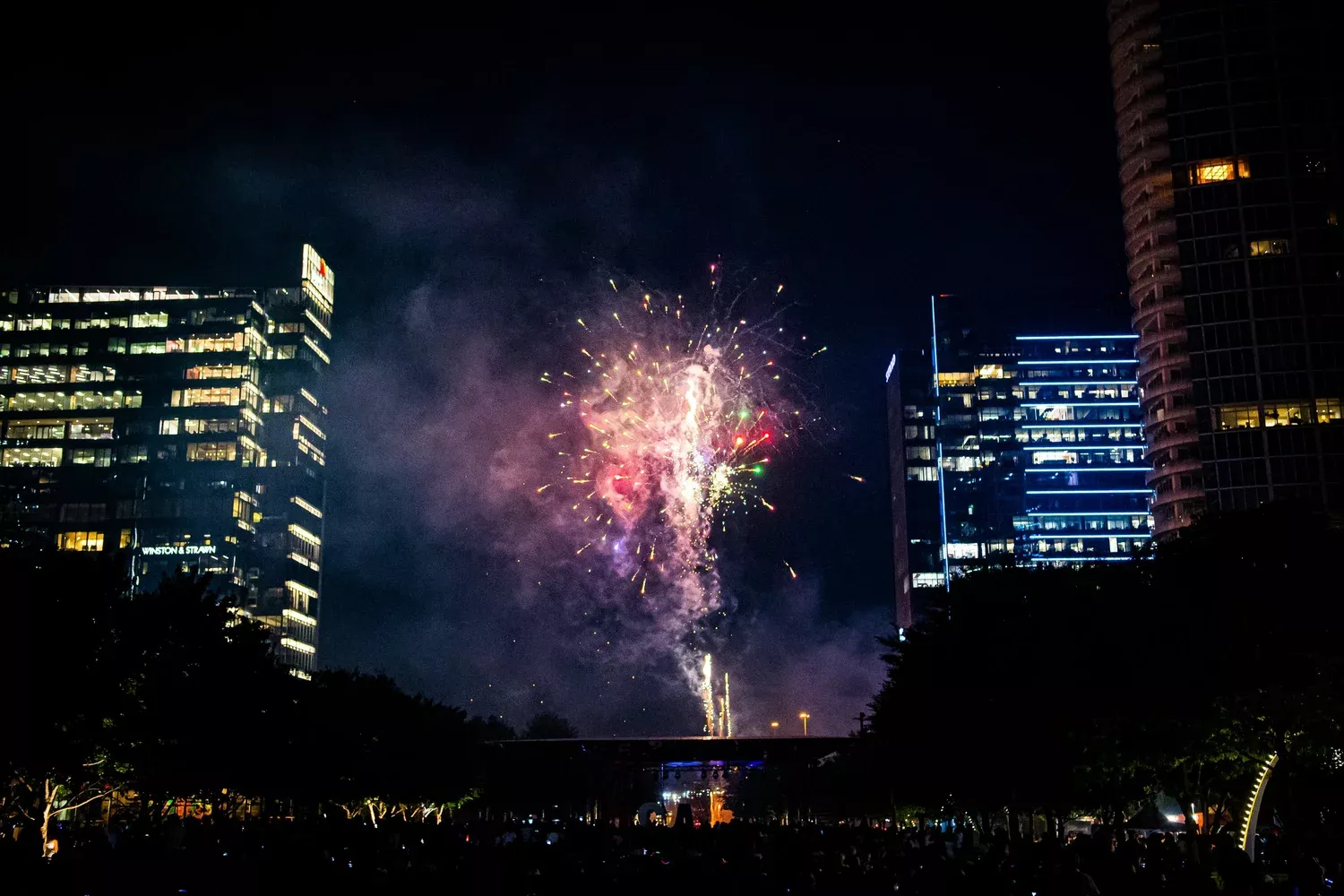 A smoky burst of red fireworks is framed by the Dallas skyline, viewed from Klyde Warren Park.